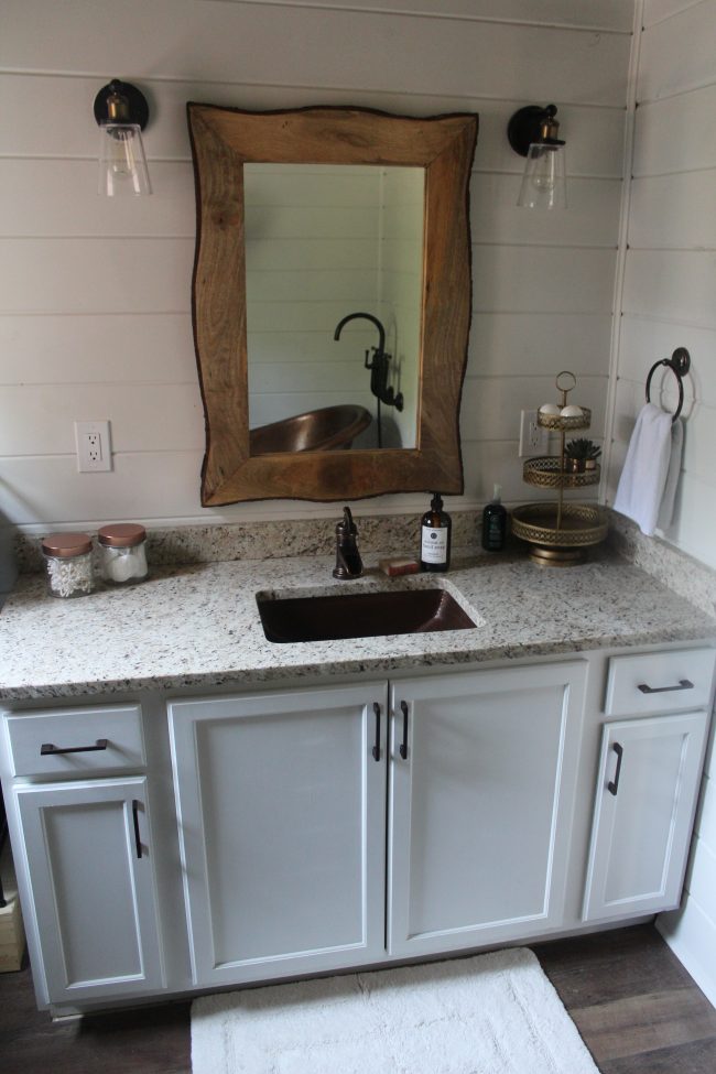 A modern farmhouse bathroom makeover - with a copper tub, copper sink, wood plank ceiling, white shiplap walls, LVT flooring, and granite counter tops.