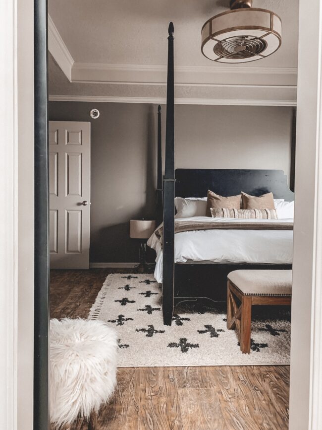 Black and white area rug in master bedroom, white bedding, black four poster bed || Neutral master bedroom design, plus the plans we have to change things up! Kansas City life, home, and style blogger Megan Wilson shares her master bedroom design plans and inspiration