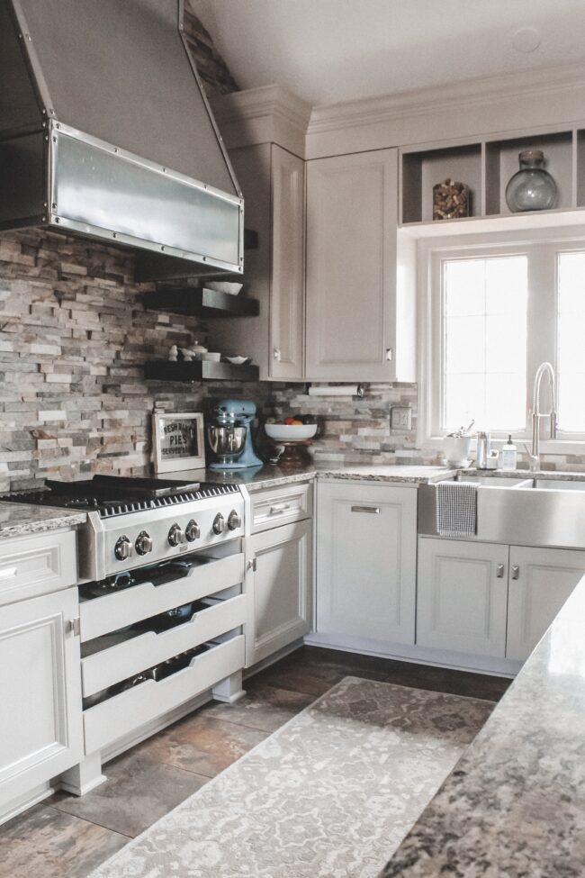 Home Tour: our rustic meets modern kitchen! Kansas City life, home, and style blogger Megan Wilson shares a tour of her new home's kitchen with stone backsplash, stainless range hood, granite and wood countertops, metal and wood accents, stainless farmhouse kitchen sink, and open shelves. 