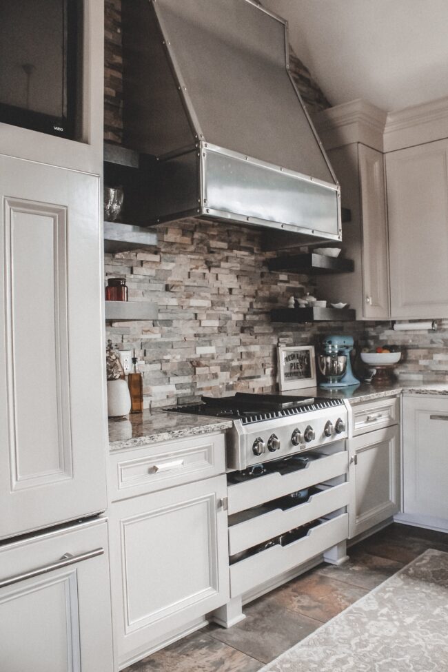 Home Tour: our rustic meets modern kitchen! Kansas City life, home, and style blogger Megan Wilson shares a tour of her new home's kitchen with stone backsplash, stainless range hood, granite and wood countertops, metal and wood accents, stainless farmhouse kitchen sink, and open shelves. 