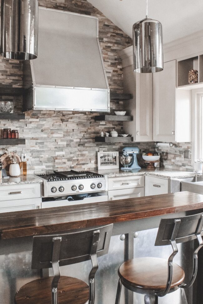 Home Tour: our rustic meets modern kitchen! Kansas City life, home, and style blogger Megan Wilson shares a tour of her new home's kitchen with pendant lights over the island, stainless range hood, stone backsplash, granite and wood countertops, metal and wood accents, stainless farmhouse kitchen sink, and open shelves. 