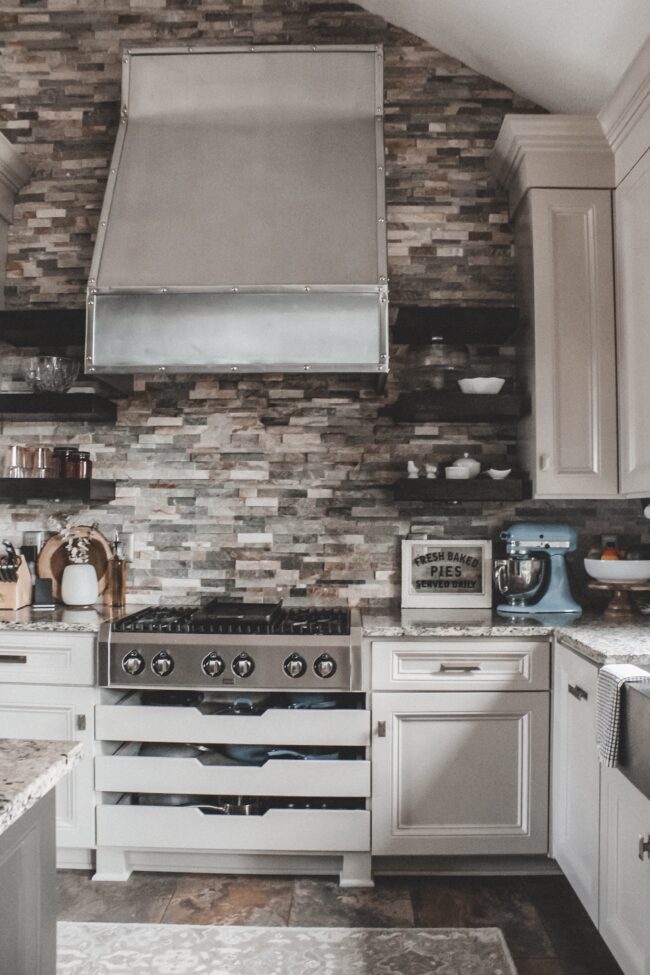 Home Tour: our rustic meets modern kitchen! Kansas City life, home, and style blogger Megan Wilson shares a tour of her new home's kitchen with stone backsplash, granite and wood countertops, stainless range hood, metal and wood accents, stainless farmhouse kitchen sink, and open shelves. 