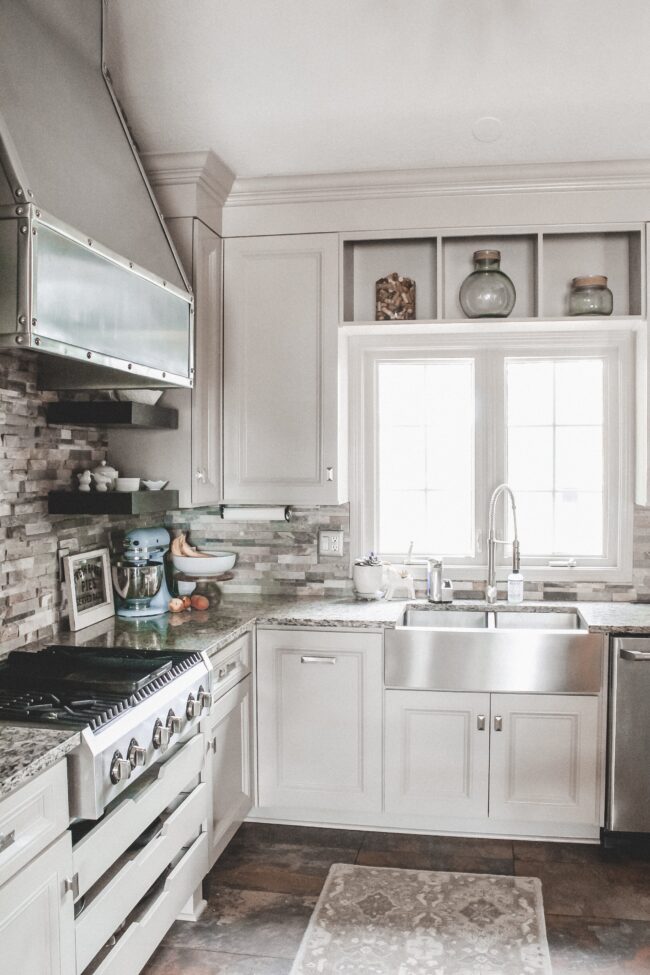 Home Tour: our rustic meets modern kitchen! Kansas City life, home, and style blogger Megan Wilson shares a tour of her new home's kitchen with stone backsplash, stainless range hood, granite and wood countertops, metal and wood accents, stainless farmhouse kitchen sink, and open shelves. 